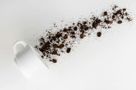 Ground coffee and coffee beans pouring out of a cup on a gray background.の写真素材