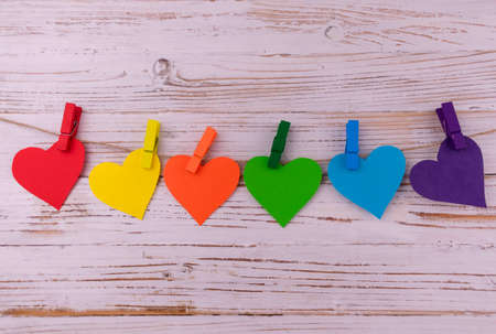 Hearts in rainbow colors hang on clothespins in a row on a wooden background. LGBT symbol. Copy space.の写真素材