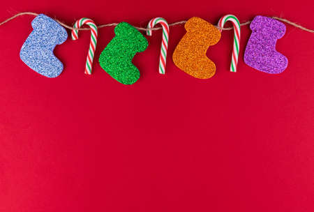 Christmas socks and candies hang on a rope on a red background. Copy space.