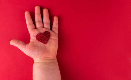 Red heart in small children's hand on a red background. Copy space.の写真素材
