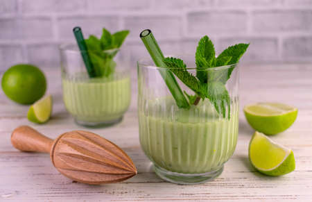 Two glasses of lime mint smoothie on a white wooden table.
