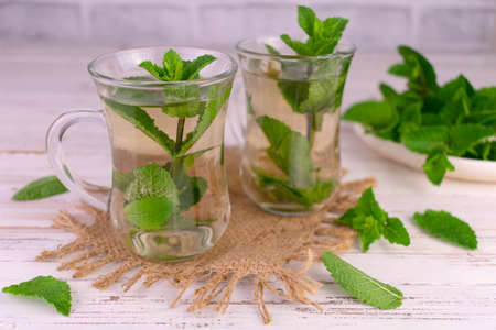 Mint tea in transparent cups on a white wooden background.
