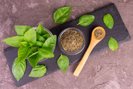 Fresh bezel leaves and dried basil on a black board. top view.