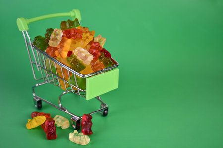 Gummy bears in a small supermarket cart on a green background.の写真素材
