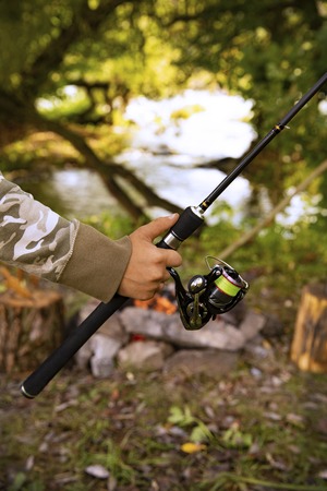A fisherman with a fishing rod. Close-up of a hand holding a spinning rod and twisting a coil. Colorful view, blurred background, selective focus.の写真素材