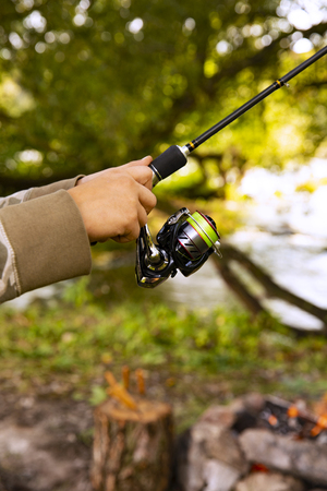 A fisherman with a fishing rod. Close-up of a hand holding a spinning rod and twisting a coil. Colorful view, blurred background, selective focus.の写真素材