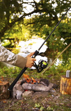 A fisherman with a fishing rod. Close-up of a hand holding a spinning rod and twisting a coil. Colorful view, blurred background, selective focus.の写真素材