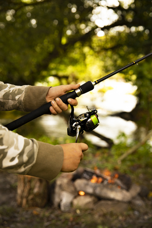 A fisherman with a fishing rod. Close-up of a hand holding a spinning rod and twisting a coil. Colorful view, blurred background, selective focus.の写真素材