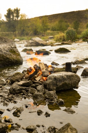 Aromatic and hot coffee on the fire. Bonfire and thermo mugs. Bonfire on the river bank.の写真素材