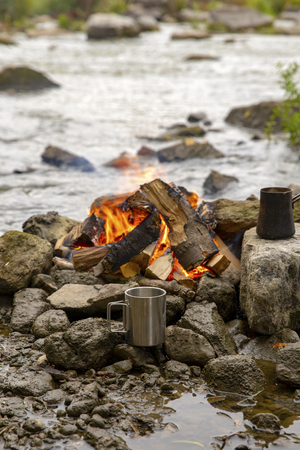 Aromatic and hot coffee on the fire. Bonfire and thermo mugs. Bonfire on the river bank.の写真素材