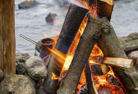 Aromatic and hot coffee on the fire. Bonfire and thermo mugs. Bonfire on the river bank.の写真素材