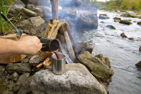 Aromatic and hot coffee on the fire. Bonfire and thermo mugs. Bonfire on the river bank.の写真素材