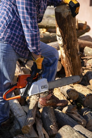 The worker works with a chainsaw. Cut the firewood ?hainsaw. Chainsaw close up. Woodcutter saws tree with chainsaw on sawmill. Chainsaw in action cutting wood. Man cutting wood with saw, dust and movements.の写真素材