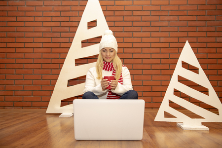 A girl is sitting with a laptop near the Christmas tree.の写真素材