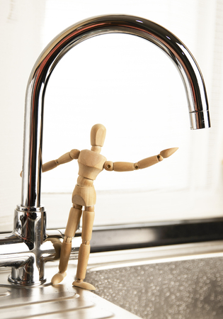 Mixer close up. Faucet with flowing water. Concept Save Energy Water. Water Drop from Tap. Mixer. Wooden mannequin. Wooden man.の写真素材