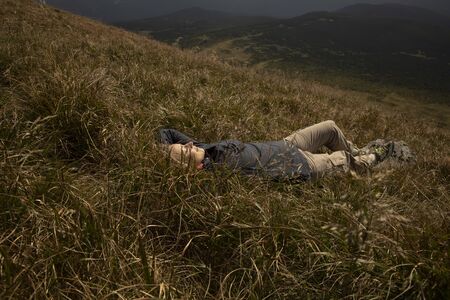Tourist girl resting in the mountains. Tourist girl lying on the grass in the mountains. Stylish traveler woman lying on grass and relaxing in mountains. Travel concept.の写真素材