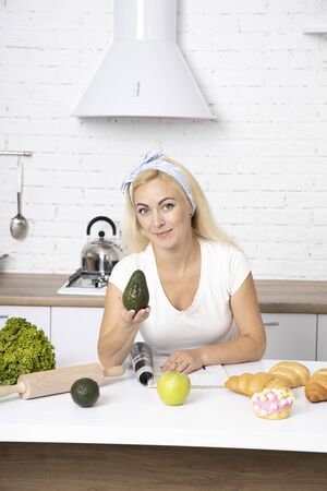 The girl is holding an avocado. Woman cutting fresh avocado at table. Breakfast of avocado.の写真素材