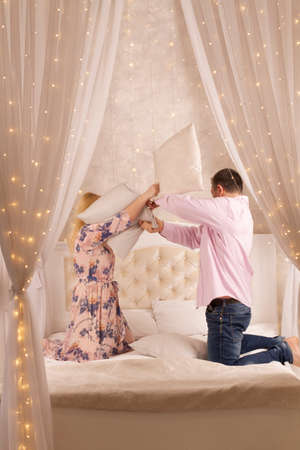 Happy playful young man and woman playing pillow fight at home, laughing loving couple having fun in bedroom, smiling wife and husband spending leisure free time together, enjoying weekendの写真素材