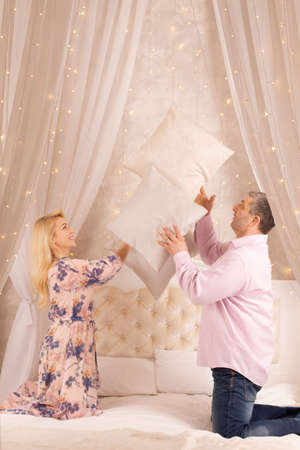 Happy playful young man and woman playing pillow fight at home, laughing loving couple having fun in bedroom, smiling wife and husband spending leisure free time together, enjoying weekendの写真素材