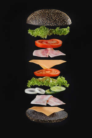 Flying burger ingredients. Delicious hamburger with flying ingredients on black background Flying burger ingredients. Burger on black background.の写真素材