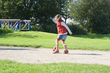 little girl playing football on the green field