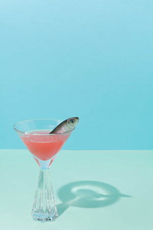 Modern conceptual setting of still life. Fish in a cocktail and a crystal glass. Pastel blue background in two shades.の写真素材