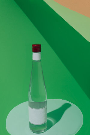 Bottle on green background and shadows. Red shutter. Blank label. Conceptual setting, minimalism.の写真素材