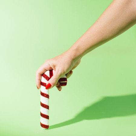 A woman's hand painted with red nail polish. She holds a Christmas tree decoration in the shape of a sassy umbrella and says Happy New Year. Pastel background.の写真素材
