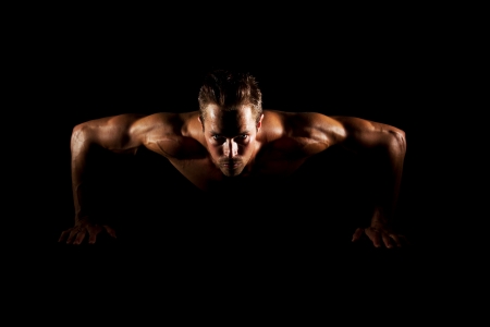 Man with focused eyes doing pushups on black backgroundの写真素材
