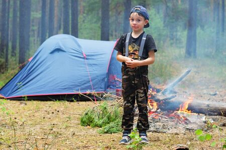 Tourist camping with tents in a pine forest. A small child-traveler on the background of a tent and a fire. Family adventure in nature.の写真素材