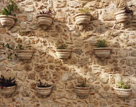 Clay stone wall made of shards and fragments of dishes and tiles. Vases pots with flowers from...