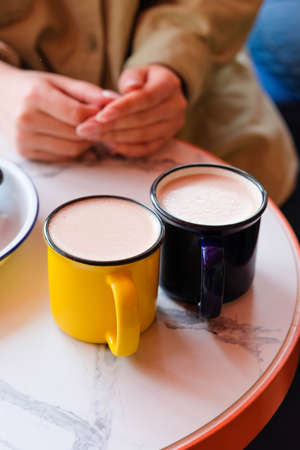 Two colored mugs with a hot drink and foam stand on the table against the background of womens hands.の写真素材