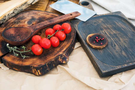 Fresh cherry tomatoes and spices on the wood and a chef's knife on the light surface of the table. Background of a modern restaurant kitchen with a copy space on a rustic cutting board, top viewの写真素材