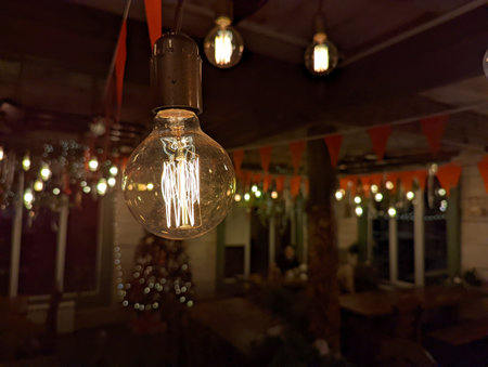 A close-up image of a hanging orange light bulb in a restaurant or cafe with a festive interior