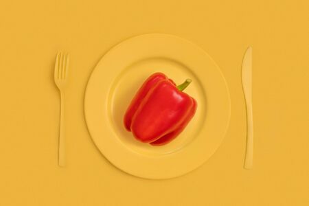 Red bell pepper on top on a yellow plate, knife and fork. On yellow background. The view from the top. Close upの写真素材