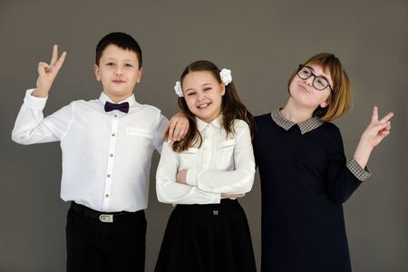 best school friends: girls and boys. Happy grinning classmates stand hugging on a gray background...