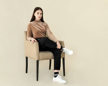 beautiful teenager girl sitting on an armchair. Emotion of calm and joy. Beige backgroundの写真素材