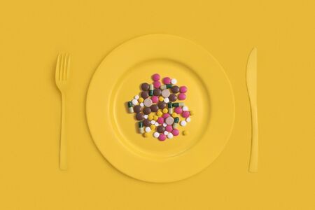 Assorted pharmaceutical medicine pills, tablets and capsules on a plate. On a yellow backgroundの写真素材