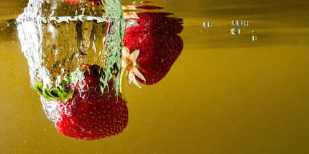 ripe strawberries fall into the water lifting splashes and air bubblesの写真素材