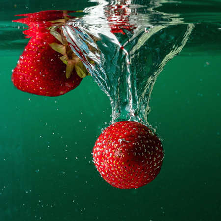 ripe strawberries fall into the water lifting splashes and air bubblesの写真素材