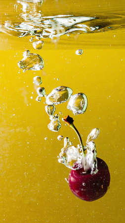 ripe cherries fall into the water raising splashes and air bubblesの写真素材