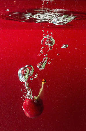 ripe cherries fall into the water raising splashes and air bubblesの写真素材