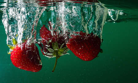 ripe strawberries fall into the water lifting splashes and air bubblesの写真素材