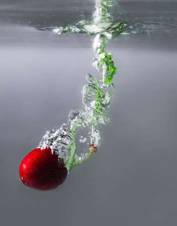 ripe cherries fall into the water raising splashes and air bubbles