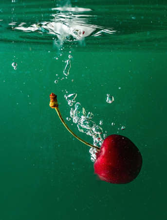 ripe cherries fall into the water raising splashes and air bubblesの写真素材