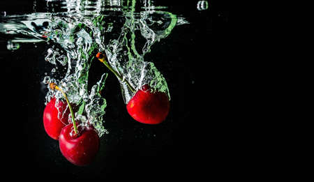 ripe cherries fall into the water raising splashes and air bubbles