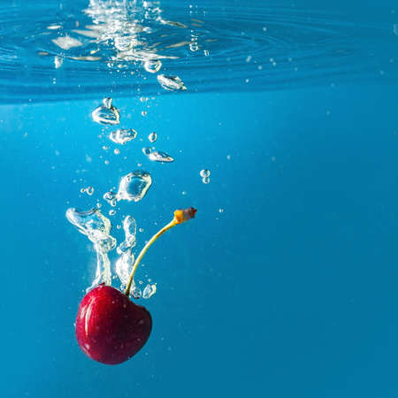 ripe cherries fall into the water raising splashes and air bubbles