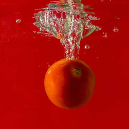 Ripe tomato falls deeply under water with a big splash.の写真素材