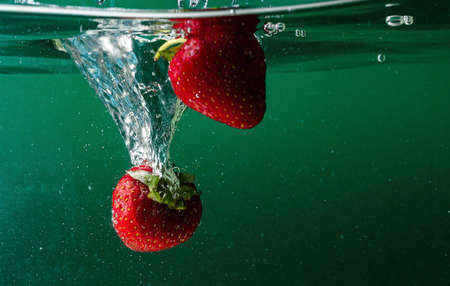 ripe strawberries fall into the water lifting splashes and air bubblesの写真素材