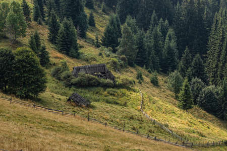 Abandoned buildings in the mountains, wooden houses against the background of rocks, the natural landscape, the beauty and majesty of green meadows and forestsの写真素材